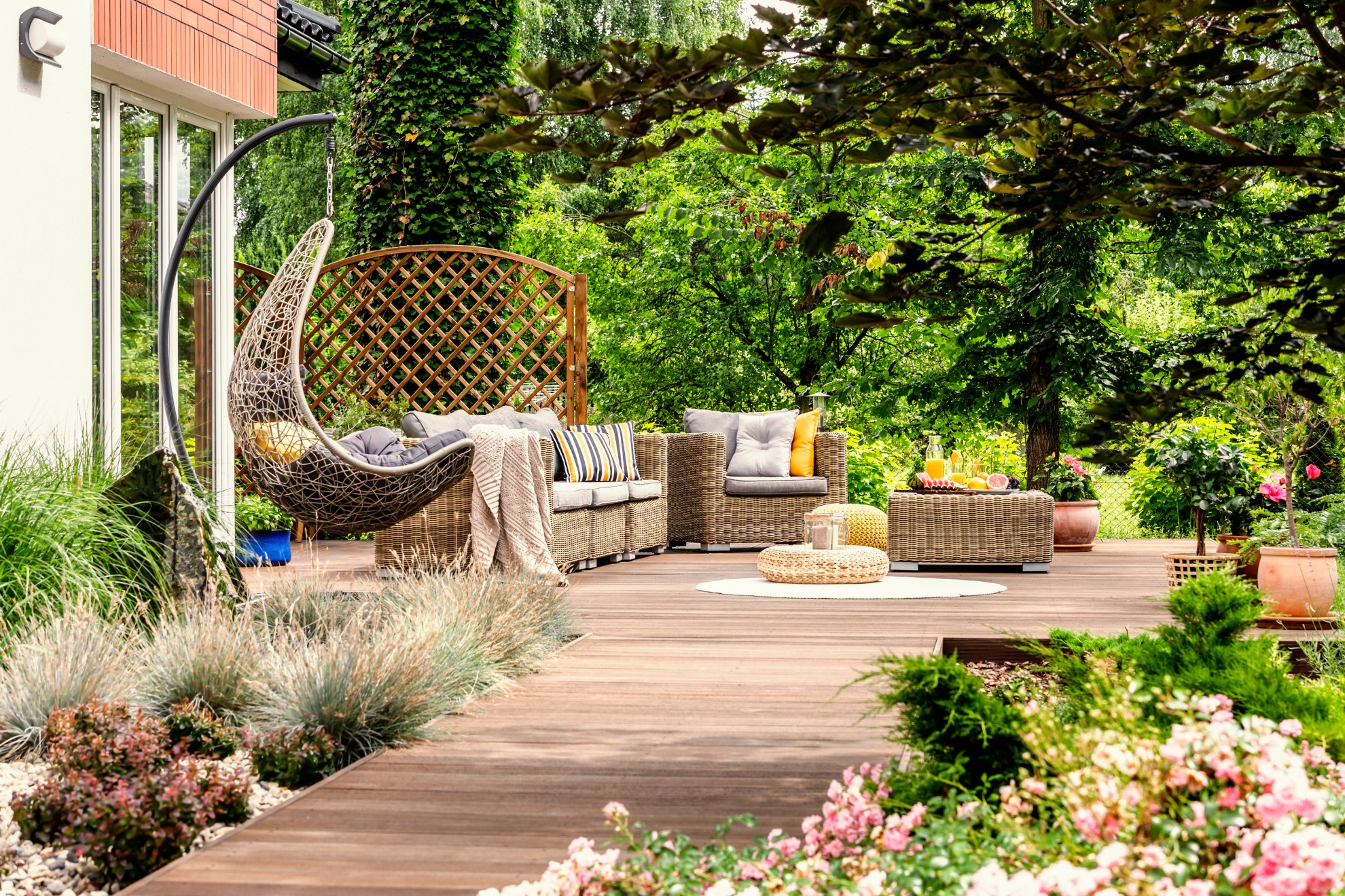 Hanging chair and pouf on wooden veranda in the middle of garden